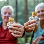 Smiling senior couple of hikers enjoying a snack break in the forest