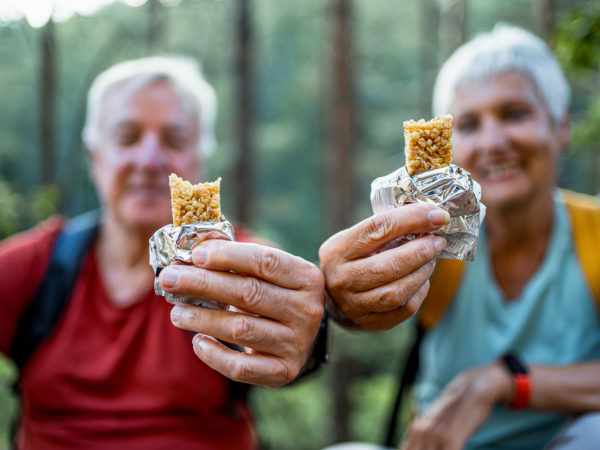 Smiling senior couple of hikers enjoying a snack break in the forest