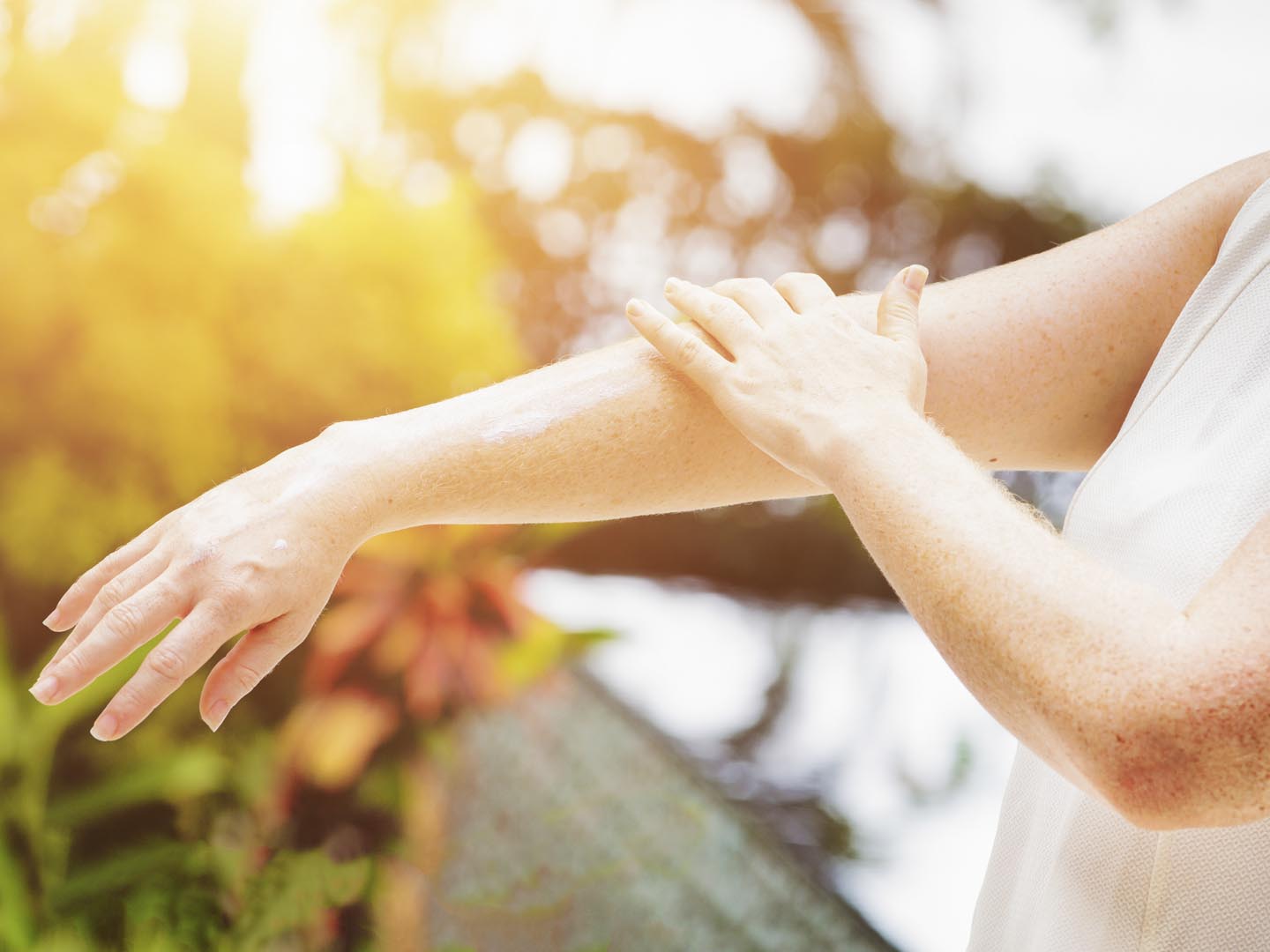 Young freckled woman applying sun screen cream on her arms while on vacations in tropical location.  Photographed in Bali, Indonesia.