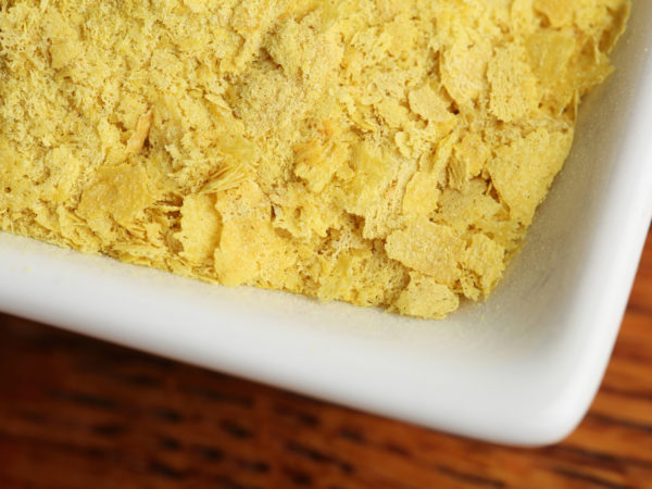 Small dish of nutritional yeast on a wooden background.  Shot in studio with a Canon 5D Mark III.