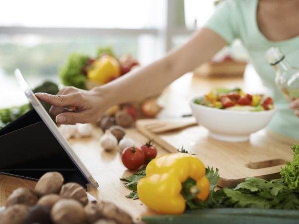 Woman checking recipe on digital tablet before seasoning salad