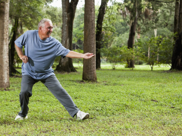 Senior man (60s) exercising in park, practicing tai chi.