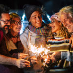 Caucasian happy family enjoy and celebrate by night with fire sparkler all together having fun - christmas and new year eve celebration for group of cheerful people mixed ages and generations